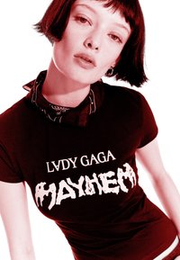Mladá osoba s krátkými tmavými vlasy, oblečená v černém tričku "Lady Gaga Mayhem" a černém vzorovaném šátku na krk, na bílém pozadí.