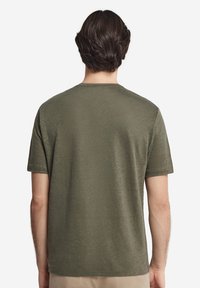 Olivgrön kortärmad T-shirt med rund halsringning och ett slätt, något texturerat tyg. Enkelt design, inga synliga logotyper eller mönster.