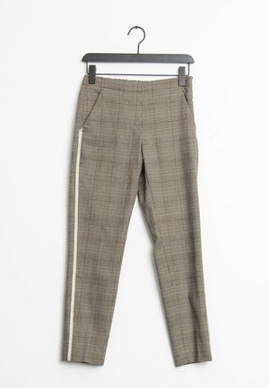 Pantalones marrones de cuadros ajustados con bolsillos delanteros y una franja lateral blanca, colgados en una percha negra sobre un fondo blanco.