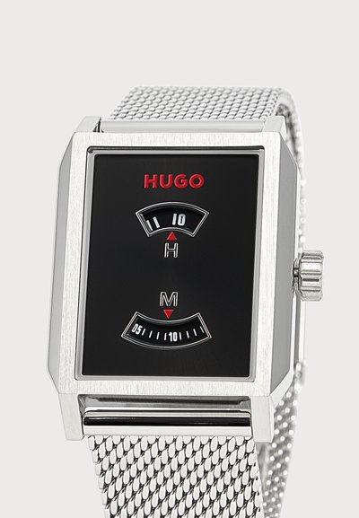 Montre rectangulaire argentée avec cadran noir, logo rouge "HUGO", affichages numériques des heures et des minutes, et bracelet en maille argentée.