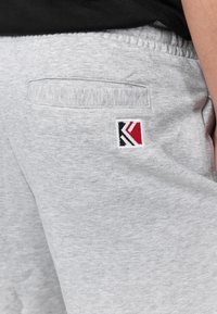 Gray sweatpants with a textured finish, featuring a small embroidered logo in red, black, and white on the back pocket. Elastic waistband.