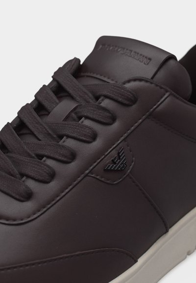 Μαύρο δερμάτινο αθλητικό παπούτσι με μαύρα κορδόνια, μικρό μεταλλικό λογότυπο αετού στο πλάι και ανοιχτόχρωμη σόλα σε κοντινή όψη.