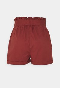 Shorts rouges avec une taille froncée et un bord à volants. Le tissu a une texture lisse, avec des ourlets roulés aux ouvertures des jambes.