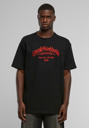 Sort bomulds T-shirt med løs pasform, korte ærmer og rød grafisk tekst. Har sætningerne "Upscale Worldwide" og "Casha Paris New York."