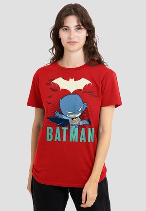 Woman wearing red t-shirt with cartoon Batman character leaping, black bats, large bat symbol, and "BATMAN" text in teal letters.