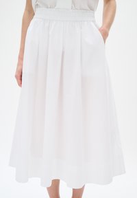 White midi skirt made of lightweight fabric, featuring an elastic waistband and side pockets. Smooth texture with a flowing silhouette.
