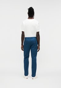 Μπλε chino με λεία υφή, σχεδιασμό με ίσια μπατζάκια και πίσω τσέπες. Συνδυασμένα με απλό λευκό μπλουζάκι και λευκά αθλητικά παπούτσια.