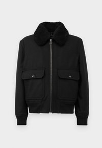 Chaqueta negra con un cuello de borreguito texturizado negro, cremallera frontal y dos bolsillos en el pecho con cierres de botón a presión. Tela suave, diseño ajustado.