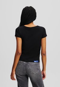 Tricou negru cu mânecă scurtă și decolteu rotund, asociat cu blugi gri din denim, care au o etichetă albastră la spate și un design clasic al buzunarelor.