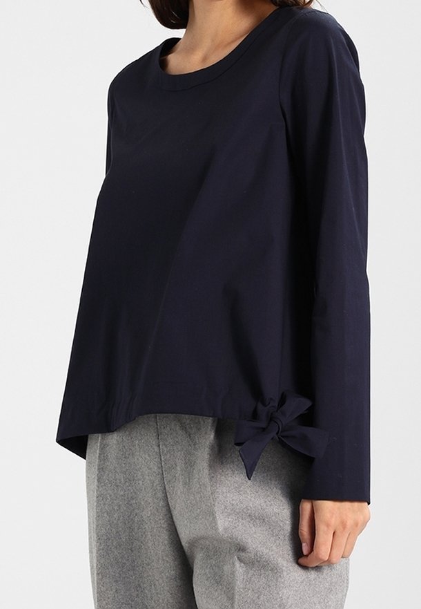 Maglia a maniche lunghe blu navy con scollo rotondo e dettaglio a fiocco laterale, abbinata a pantaloni grigi chiari con un design rilassato e fluido.