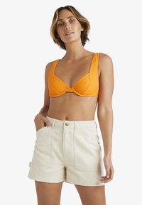 Orange ribbad bikiniöverdel med breda band och ett samlat center, matchad med högmidjade krämfärgade shorts med sidofickor och knappstängning.