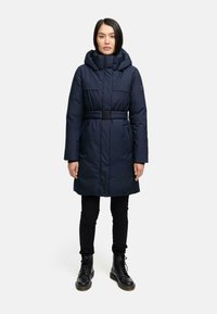 Navy blue puffer coat with a hood and belted waist; features two side pockets and a smooth texture. Black skinny pants and boots complete the outfit.