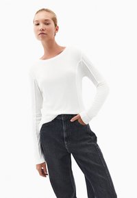 Biała koszula z długim rękawem i okrągłym dekoltem, z przeszyciami, w połączeniu z czarnymi dżinsami o wysokim stanie. Gładka tekstura, nowoczesny krój.