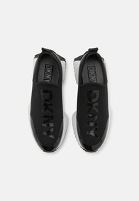 Sorte slip-on joggesko med et glatt tekstil-overdel, blanke svarte detaljer og fremtredende DKNY-logo. Har en hvit såle for kontrast.