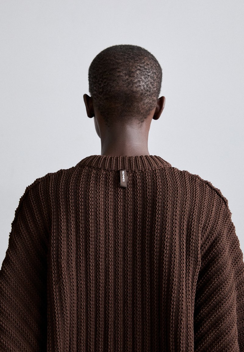 Brown knit sweater with a ribbed texture. Features a wide crew neckline and a sewn label at the back. Design has slightly loose fit.