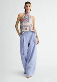 Wielokolorowy top na szyi z jedwabiu z kwiatowym i geometrycznym wzorem, zestawiony z jasnoniebieskimi spodniami typu wide-leg uszytymi z miękkiego materiału.