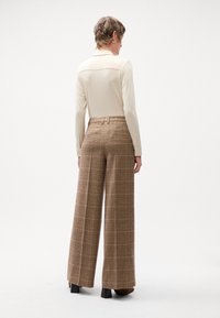 Bruine geruite wijde broek gemaakt van een gestructureerde stof, gecombineerd met een lichtgekleurde lange mouwen blouse. Zichtbare achterzakken en riemlussen.