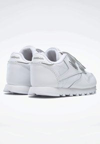 Hvit lær sneakers med en glatt overflate, med et metallisk sølvfargeaccent, borrelås og en teksturert gummisåle.