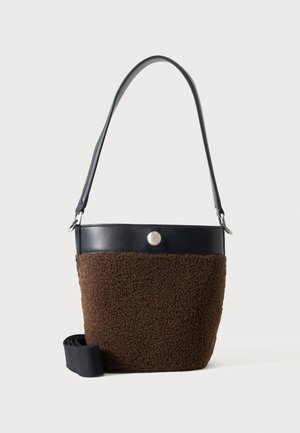 Braune strukturierte Bucket Bag mit schwarzem Lederoberrand, silbernem Knopfdetail und schwarzem Schulterriemen auf weißem Hintergrund.