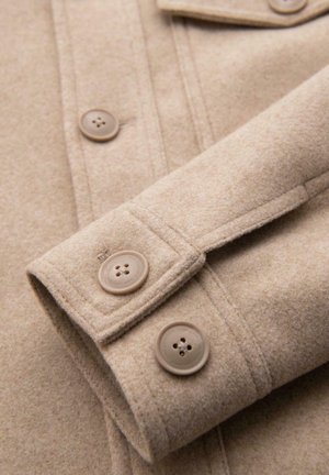 Beige wollen jassectie met een close-up van de manchette, met twee ronde knopen en een zachte, gestructureerde afwerking.