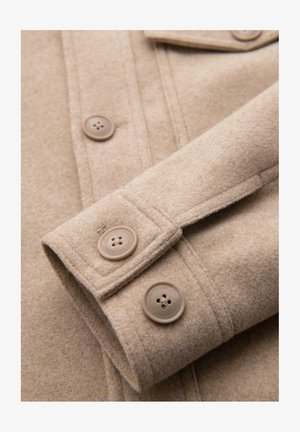 Section d'un manteau en laine beige avec un gros plan sur le poignet, présentant deux boutons ronds et une finition douce et texturée.