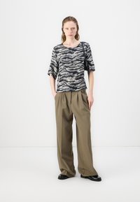 Svart og gråstripet kortermet topp kombinert med løse khaki-bukser. Modellen har på seg svarte sko og bærer en liten svart veske.