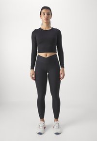 Black long-sleeve crop top and high-waisted leggings, both made of stretchy material, paired with white athletic shoes.