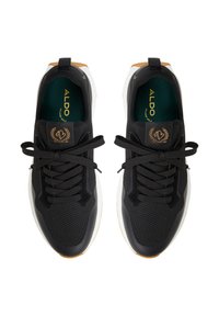 Chaussures de sport noires avec un dessus en maille texturée, des lacets noirs et une semelle intermédiaire blanche, ornées d'un logo accent brun sur la languette.