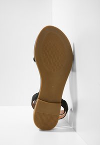 Czarny sandał z elastyczną, brązową gumową podeszwą, cechujący się gładką skórzaną cholewką i cienkimi paskami. Rozmiar 37 wydrukowany na podeszwie.