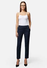 Granatowe spodni z dopasowanym krojem, z przednimi kieszeniami i zapięciem na guzik, zestawione z białą kamizelką. Gładka tekstura materiału.