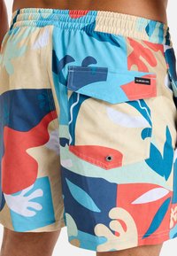 Bunte Badeshorts mit einer Mischung aus blauen, roten und beigen abstrakten Formen. Verfügt über einen elastischen Bund und eine aufgesetzte Tasche mit Druckknopfverschluss.