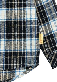 Camicia a quadri caratterizzata da una combinazione di colori neri, blu, beige e bianchi. Realizzata in tessuto morbido con un dettaglio dell'etichetta sull'orlo.