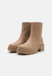 Botines beige hechos de cuero suave, con punta redondeada y cremallera lateral. Suela gruesa con ranuras texturizadas para mayor agarre.