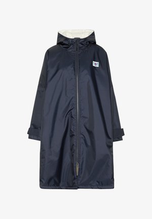 Person, die einen dunklen Kapuzenmantel mit einer grünen und pinken Grafik eines Tauchers und dem Text „Since 1982 Chill See Active Wear“ auf dem Rücken trägt.