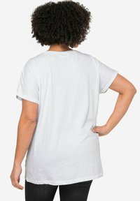 Witte korte mouwen t-shirt met omgeslagen mouwen, losse pasvorm en een langere zoom aan de achterkant. Gladde stoftextuur.