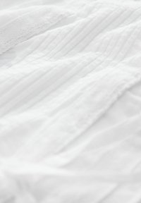 Tissu texturé blanc arborant des rayures subtiles et une qualité douce, légèrement transparente. Matériau léger et lisse avec des détails superposés.