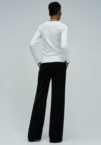 Top blanco de manga larga acanalado combinado con pantalones negros de pierna ancha. Top ajustado con cuello redondo, tejido suave y mínimos adornos.