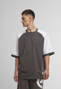 Donkergrijs t-shirt met korte mouwen, witte raglanmouwen en zwarte trim, voorzien van een logo aan de onderkant en een ontspannen pasvorm.
