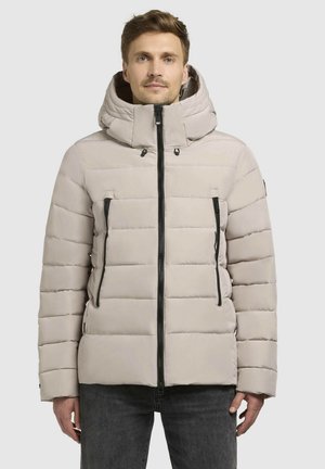 Lichtbeige pufferjack met capuchon, voorzien van zwarte ritsen, een rechthoekig quiltpatroon en twee voorzakken met rits.