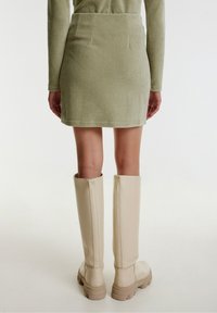 Mini-jupe en corduroy côtelé vert associée à des bottes en cuir beige hautes jusqu'aux genoux ; la jupe présente une coupe ajustée et des bords ourlés.