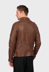 Giacca in pelle marrone con una texture liscia, colletto classico e cuciture strutturate. Presenta una chiusura a bottone ai polsini e una vestibilità su misura.