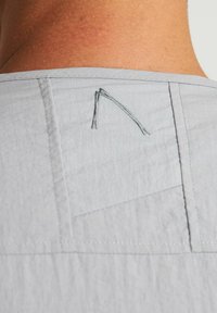 Dettaglio di una camicia grigio chiaro mostrato vicino alla parte posteriore del collo, con texture sottili, un disegno a triangolo cucito e rifinitura delle cuciture curate.