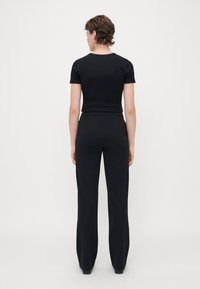 Svart tettsittende t-skjorte og høyt liv bukser laget av glatt, elastisk stoff. Korte ermer og rund hals, minimalistisk design.