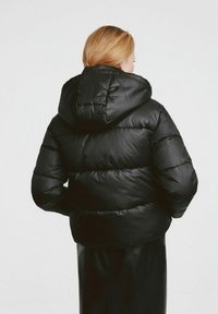 Czarna kurtka puchowa z kapturem, wyróżniająca się pikowanym wzorem i grubą izolacją. Materiał wydaje się błyszczący i gładki.