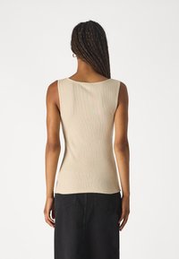 Débardeur beige côtelé avec un col arrondi, une coupe ajustée et un ourlet légèrement courbé. Associé à une jupe en jean noire.