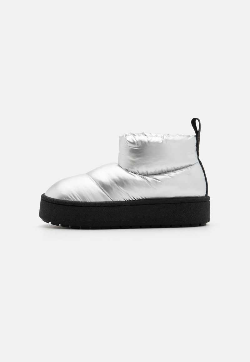 Strieborná parka ankle boot s okrúhlou špičkou, čiernou platformovou podrážkou a elastickým vrchom. Obsahuje prešité detaily na vrchnej strane.