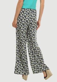 Mujer vistiendo pantalones de pierna ancha navy con estampado de margaritas blancas, blusa verde azulado y sandalias de cuña beige, vista desde la espalda.