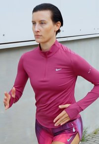 Sportkleding met een aansluitend, lang mouw, ritsnek top in roze, gecombineerd met meerkleurige shorts, ontworpen voor actieve gebruik.