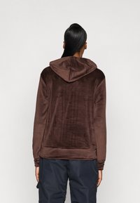 Brauner Fleece-Hoodie mit großzügiger Kapuze und langen Ärmeln, der eine weiche Textur und minimale Nähte am Saum und den Bündchen aufweist.