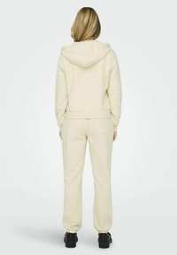 Felpa e pantaloni della tuta color crema realizzati in tessuto morbido, con una vestibilità comoda, polsini a coste e una tasca posteriore singola sui pantaloni.